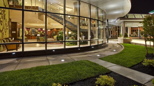 Un hotel moderno con fachada de vidrio curvada, una escalera central e interior bien iluminado.