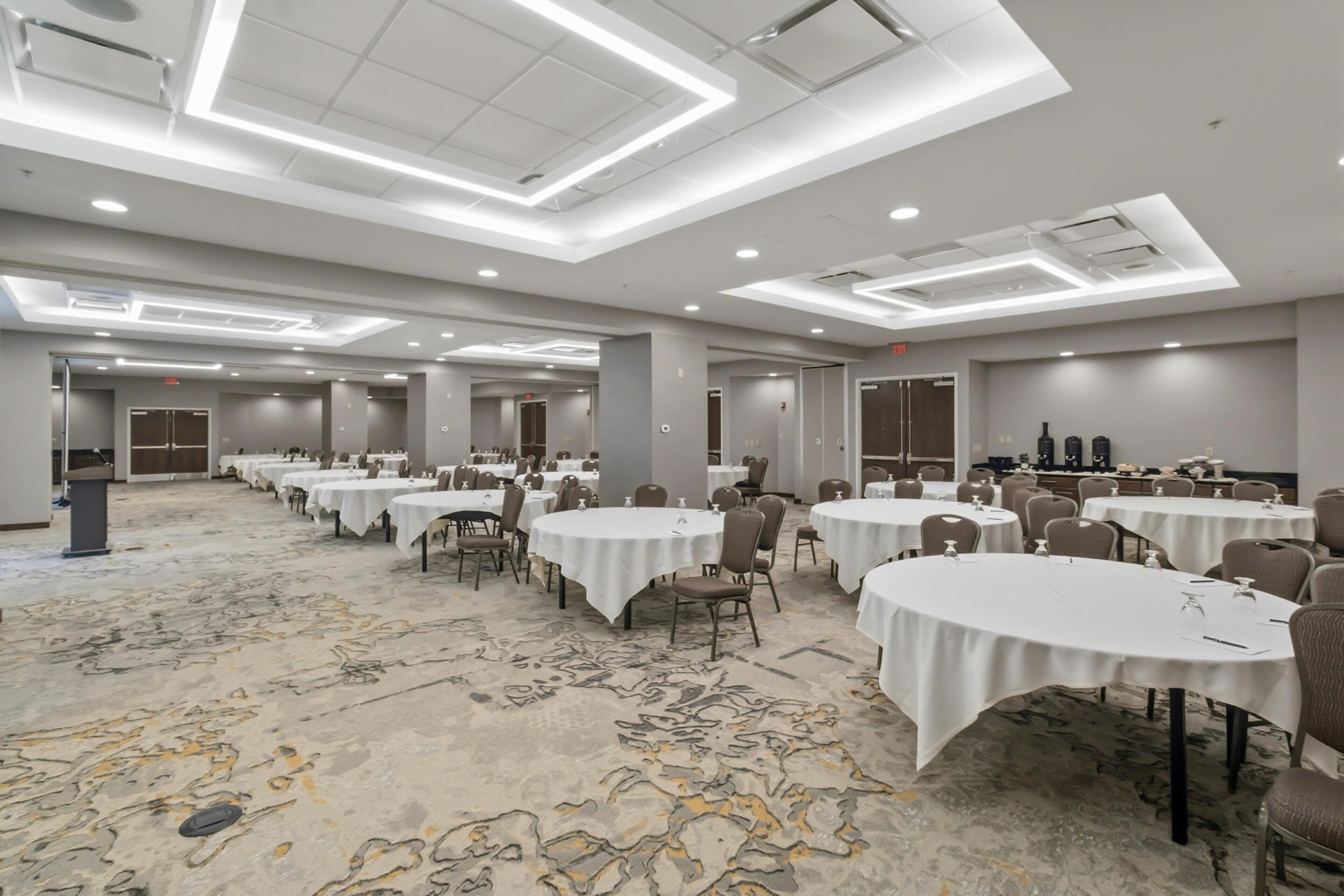 Un salón de conferencias amplio con varias mesas y sillas, un atril y una zona de escenario.