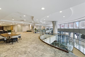 A spacious lobby with a marble floor, a central table with chairs, a staircase, and a glass railing overlooking a cityscape. - Embassy Suites Buffalo (Buffalo)