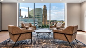 Un salón de conferencias con dos sillas y una mesa, ventanas amplias con vistas a la ciudad y una alfombra estampada.