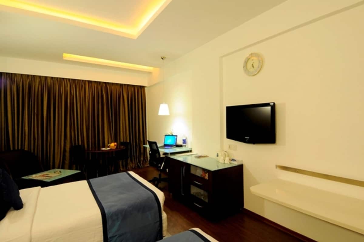 A hotel room with a bed, desk, chair, and a flat-screen TV mounted on the wall.