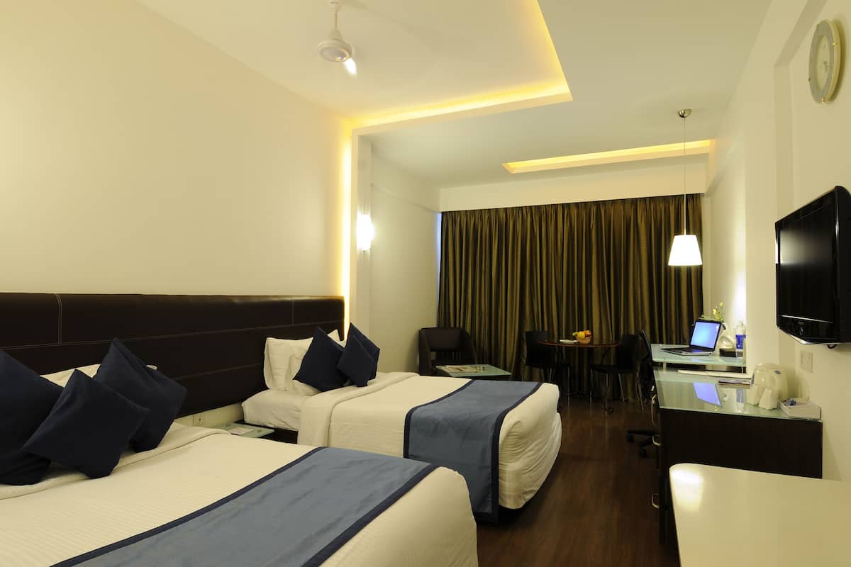 A hotel room with two beds, a desk with a laptop, a coffee maker, and a TV on the wall.