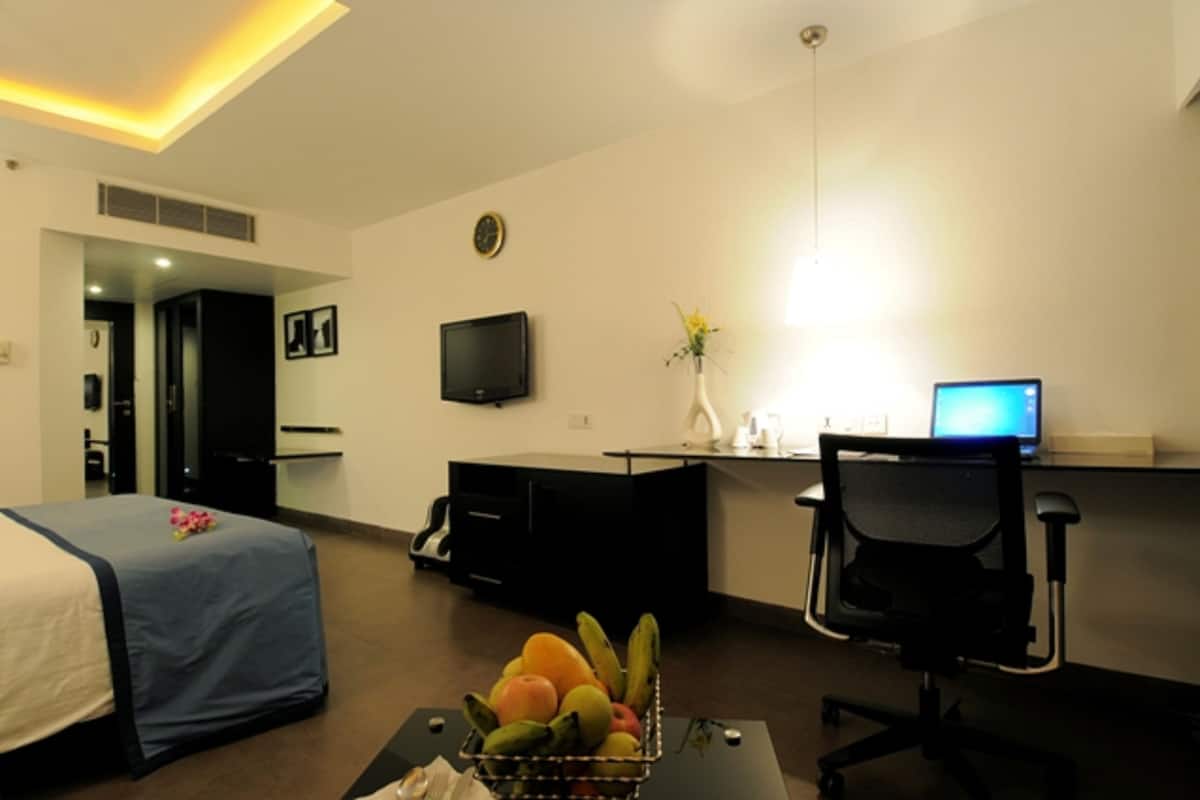 A hotel room with a bed, desk, chair, and a fruit basket.