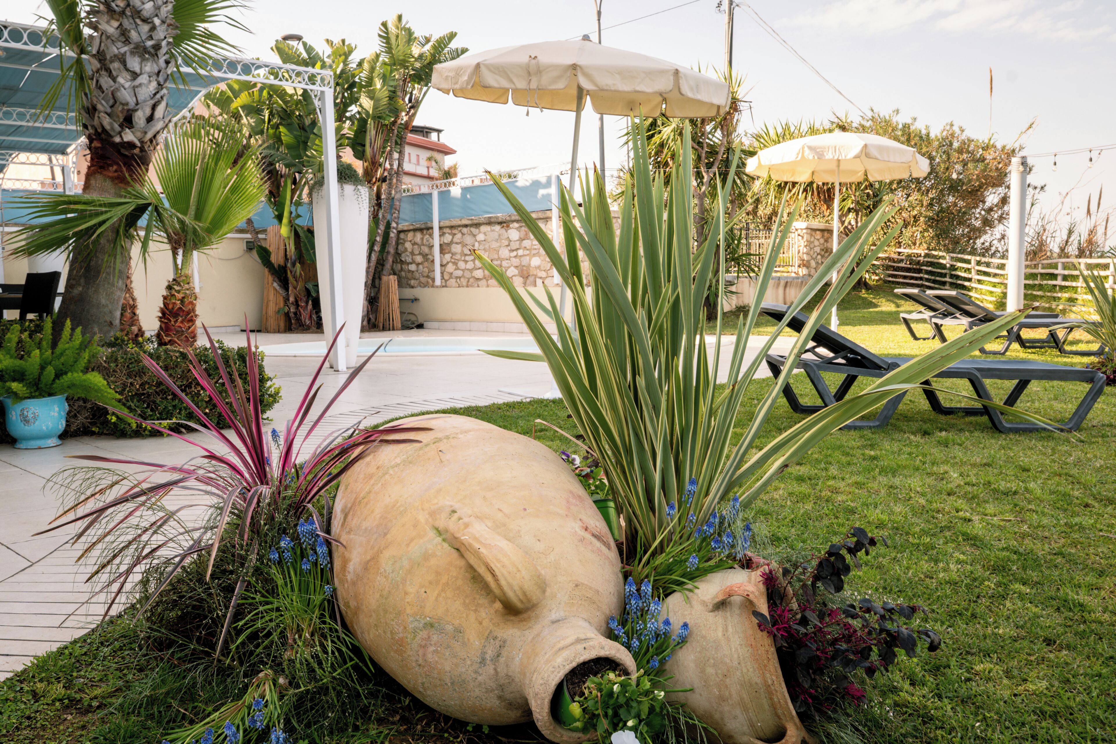 Ein Garten mit großen Dekorationsgefäßen, einem Pool und Liegestühlen.