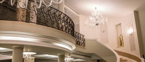 A grand staircase with a curved design, ornate railings, and multiple chandeliers.
