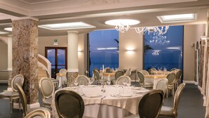 A formal dining room with marble columns, elegant chandeliers, and a view of the ocean.