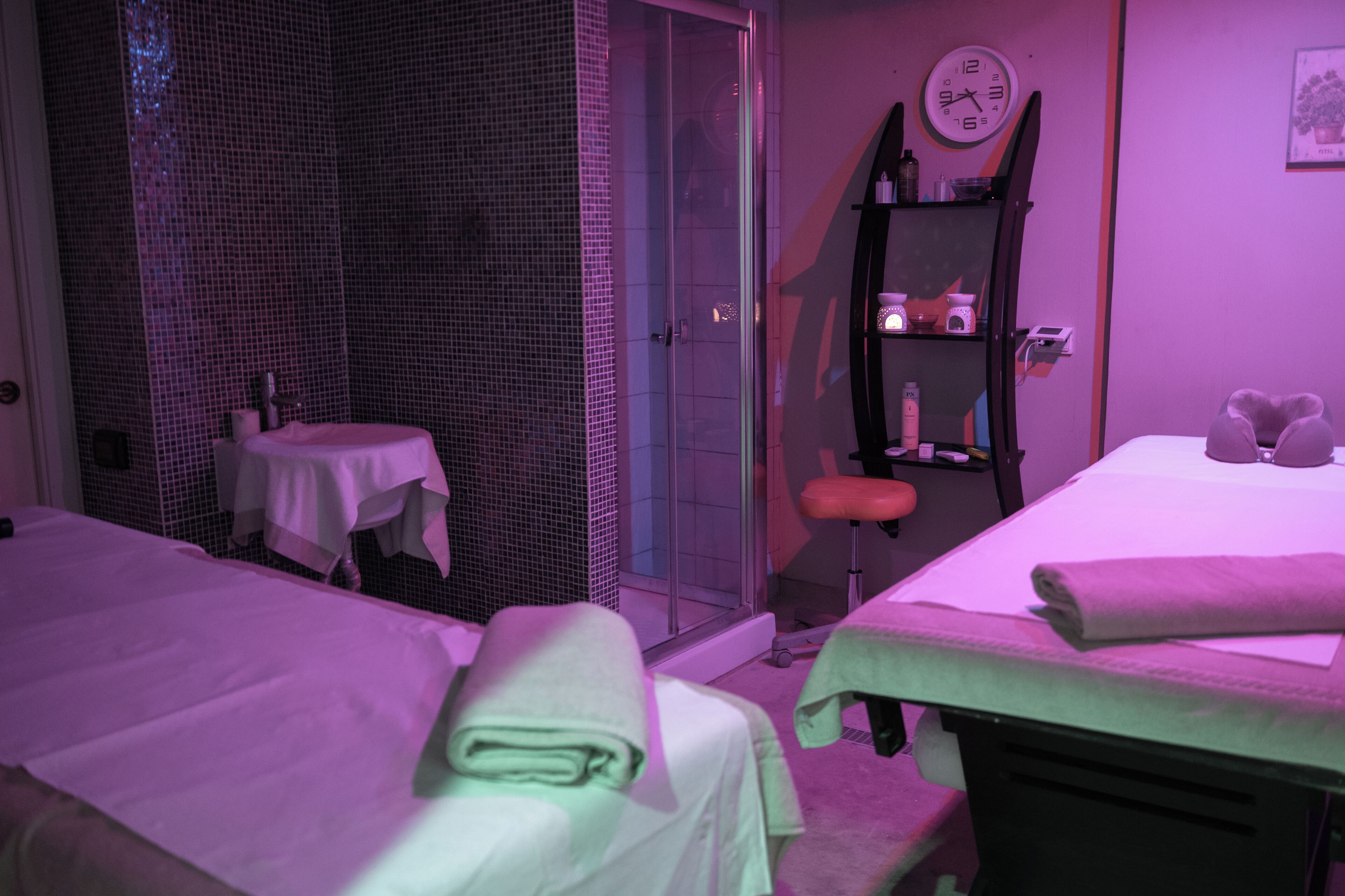 Une chambre avec deux lits, une petite table, une étagère avec des articles de toilette et une porte en verre donnant sur un espace douche.