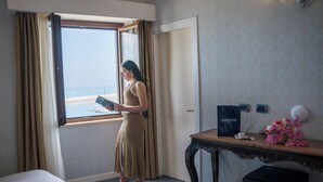A hotel room with a bed, a desk with a computer, a trash bin, and a window with curtains.
