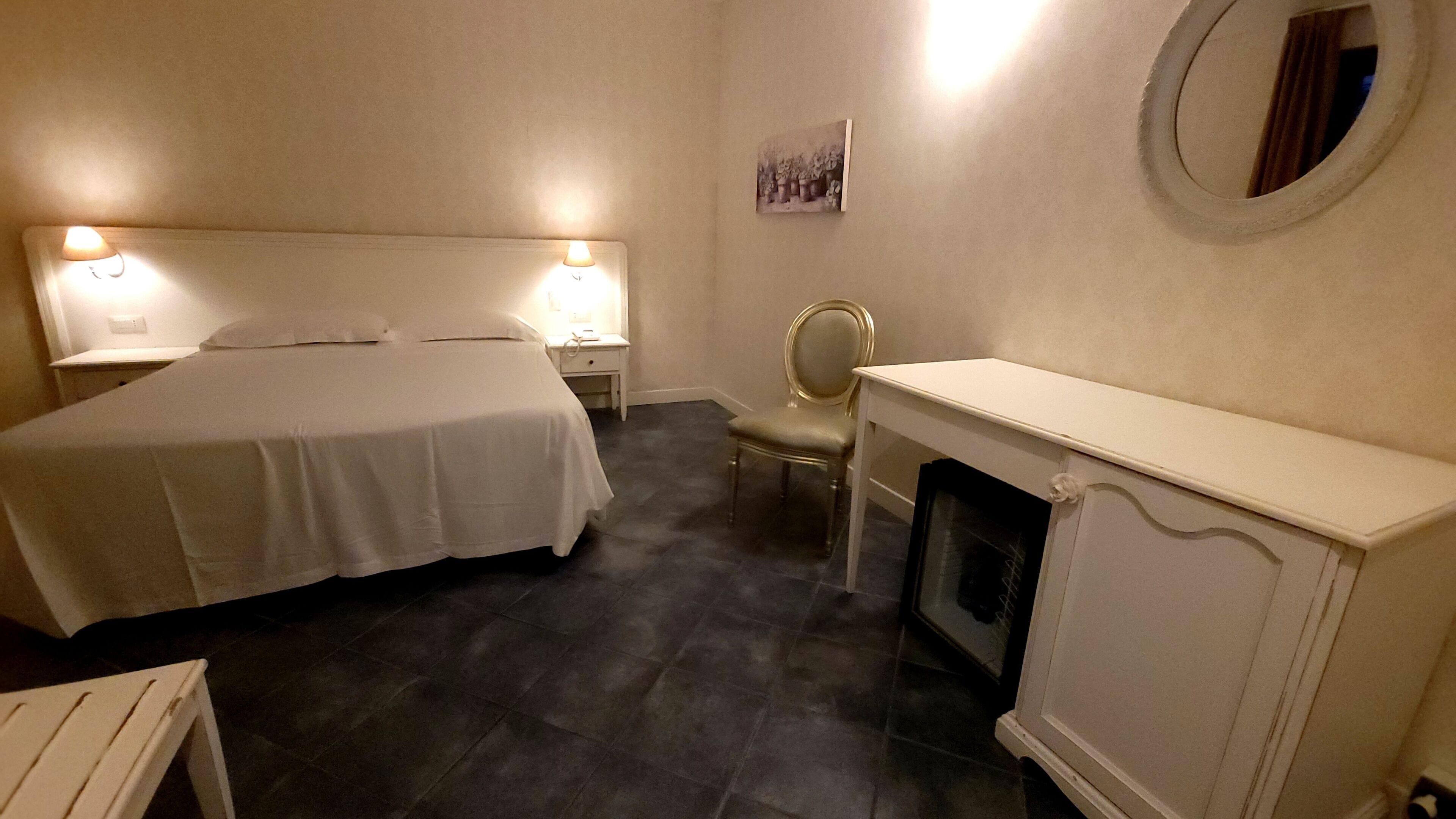Une chambre à coucher avec un lit, des lampes de chevet, une chaise, une cheminée et un miroir fixé au mur.