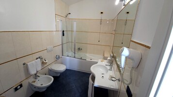 Un ba ño con bañera, dos lavamanos, un bidé, inodoro y secador de pelo, además de un espejo.