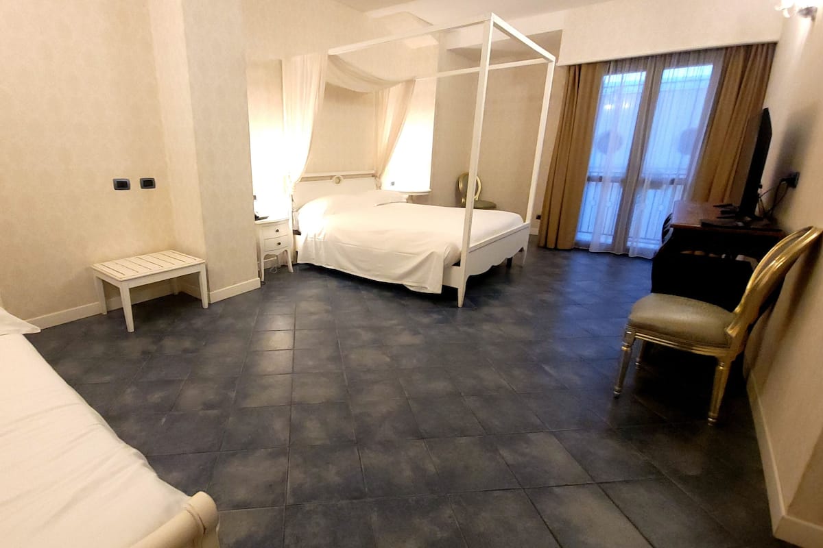 Ein Hotelzimmer mit Himmelbett, Nachttisch, Sessel und Schreibtisch mit Lampe.