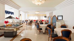 A spacious dining area with multiple tables and chairs, a central chandelier, and a buffet setup. - Hotel City (Montesilvano)