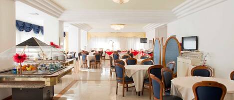 A spacious dining area with multiple tables and chairs, a central chandelier, and a buffet setup.