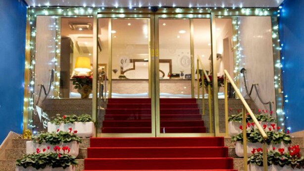 A hotel entrance with a red carpet leading to a staircase, potted plants, and a glass door entrance. - Hotel City (Montesilvano)