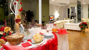 A well-lit room with a dining table set for a meal, featuring various dishes and a television in the background.