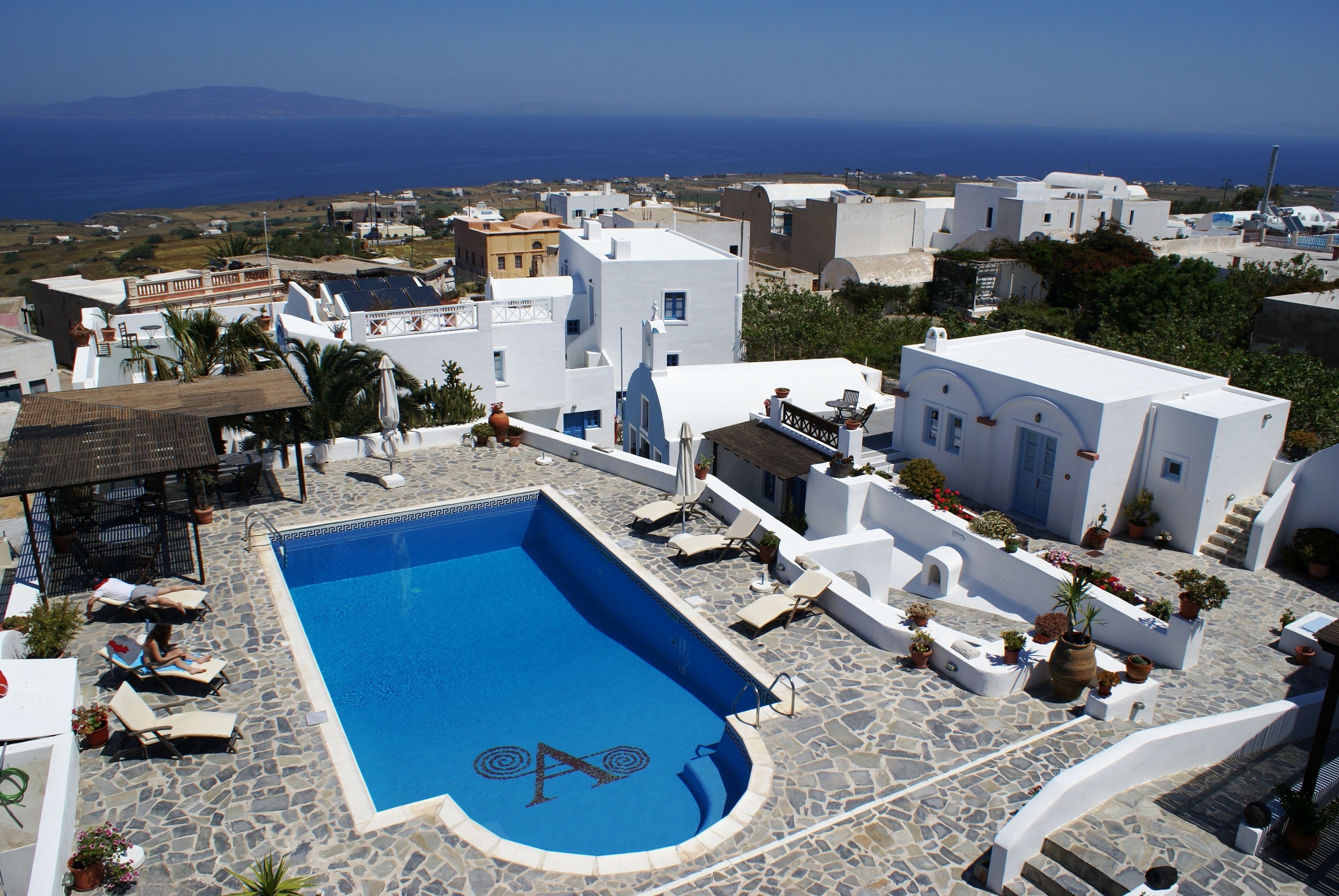 Una piscina en la azotea con borde infinito azul, rodeada de edificios blancos y vista despejada al mar.