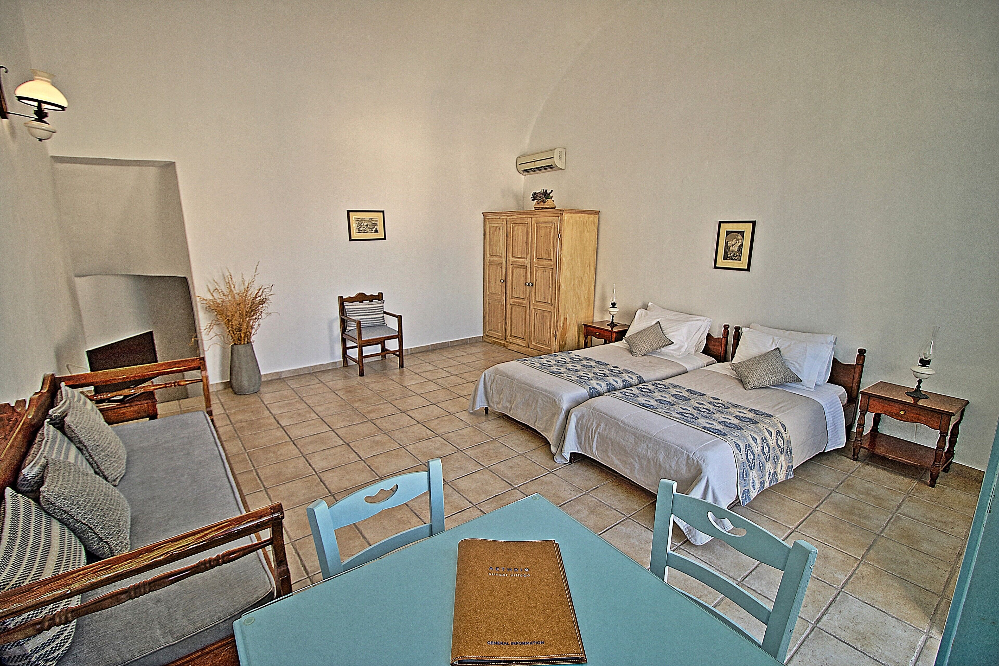 A bedroom with two beds, a sofa, a dining table, and a cabinet.