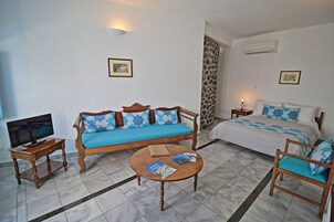 A hotel room with a sofa, a bed, a television, a coffee table, and a chair.