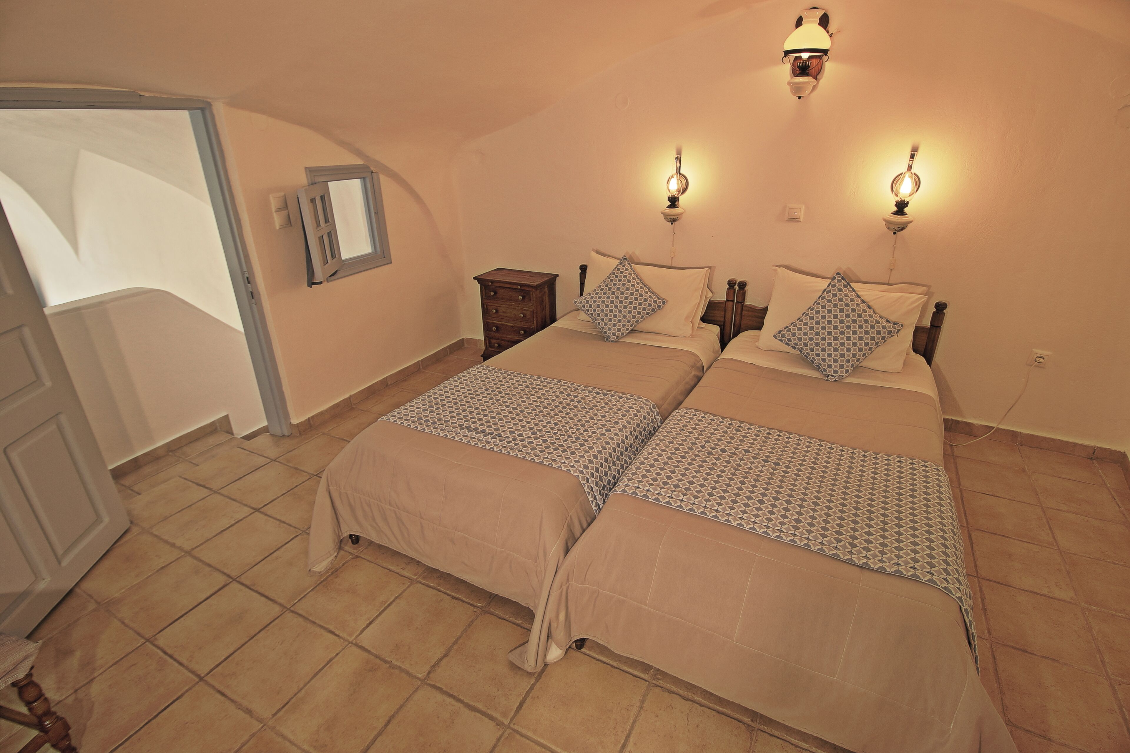 A bedroom with two beds, a wooden nightstand, a small dresser, and a wall-mounted light fixture.