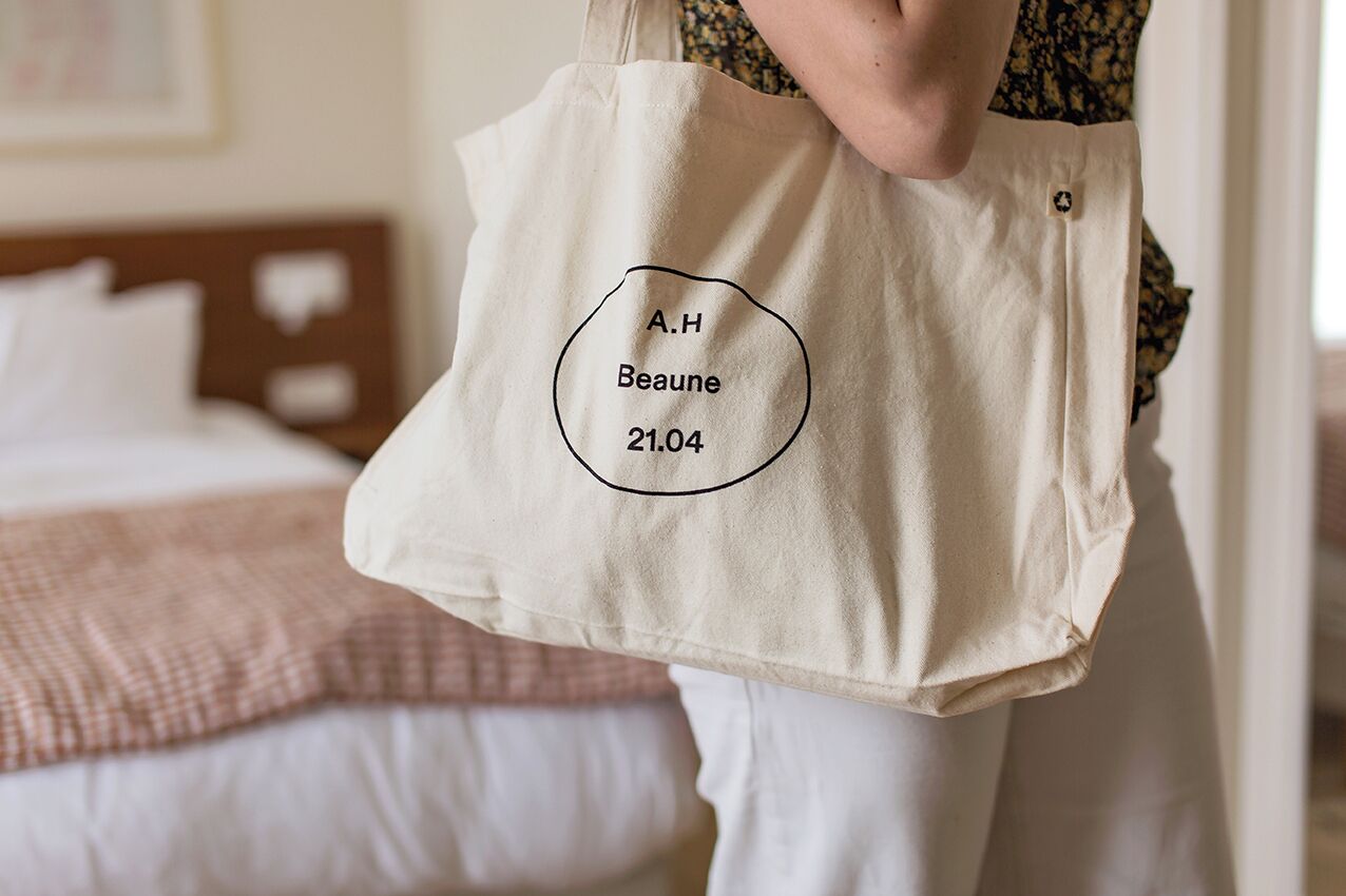 A person holding a beige tote bag with a name and date printed on it.