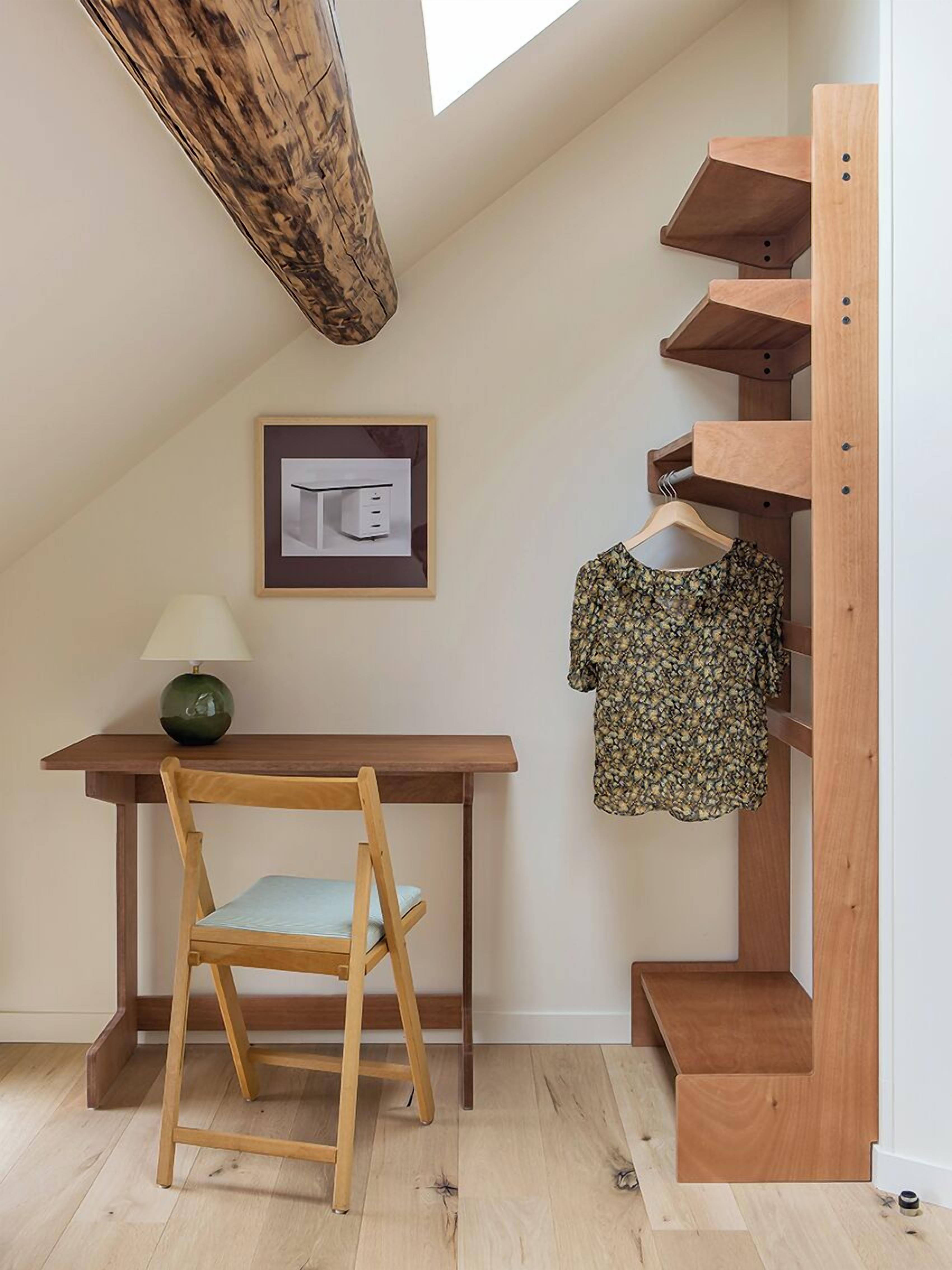 A room with a wooden desk, a chair, a hanging clothes rack, and a framed picture on the wall.