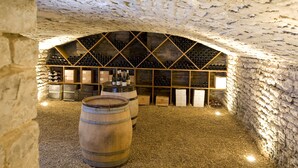A wine cellar with wooden barrels, wine racks, and a stone wall. - Alfred Hotels Beaune La Madeleine (Beaune)
