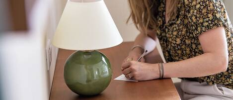 Una persona sentada a una mesa de madera, con una lámpara verde y otra blanca, escribiendo sobre un papel.