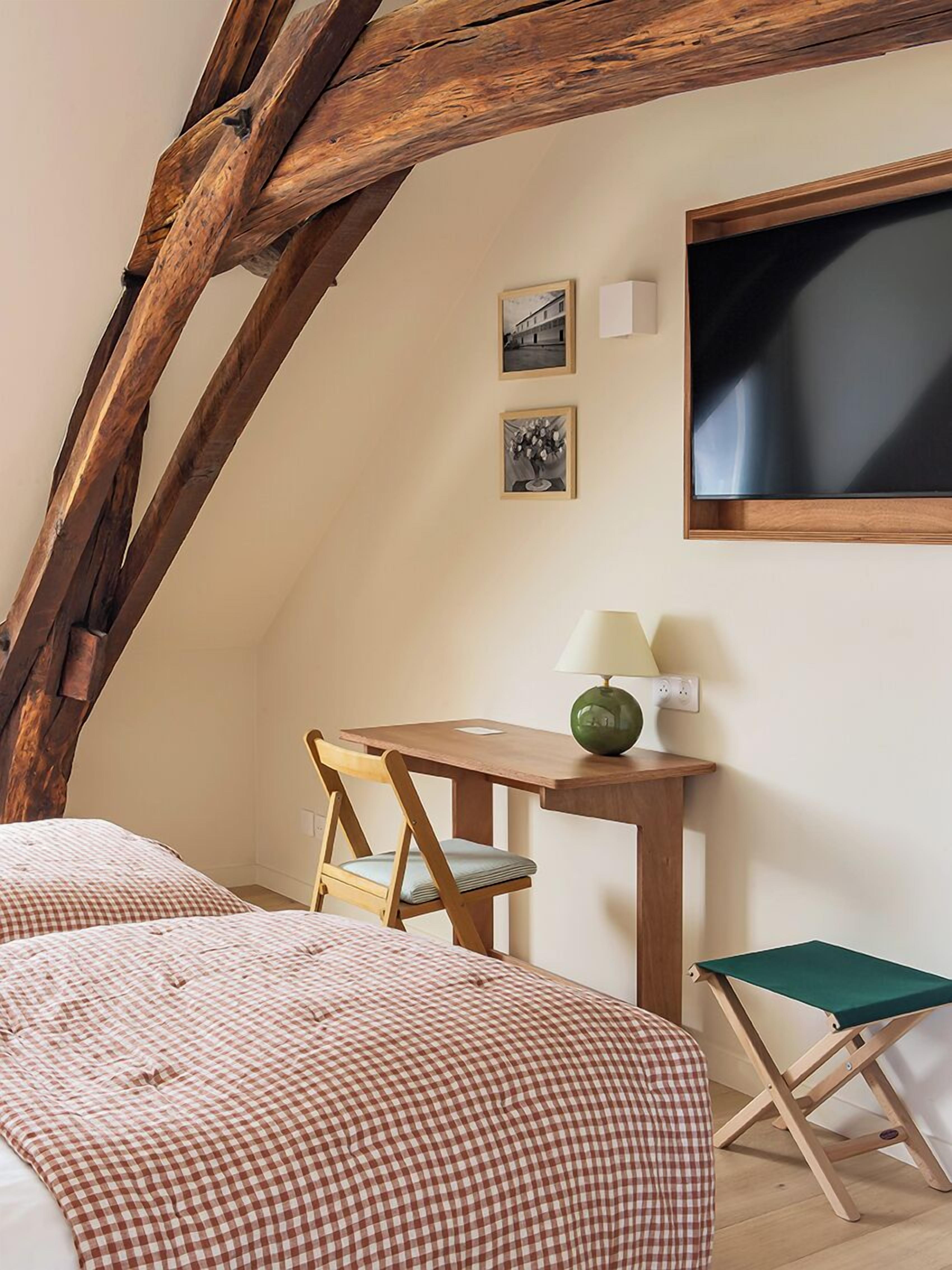 A cozy bedroom with a checkered bedspread, a wooden desk with a lamp, and a green folding chair.
