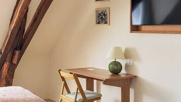 A cozy bedroom with a checkered bedspread, a wooden desk with a lamp, and a green folding chair.