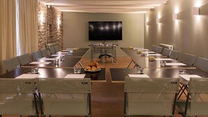 A conference room with a long table, chairs, a television, and a stone wall. - Alfred Hotels Beaune La Madeleine (Beaune)