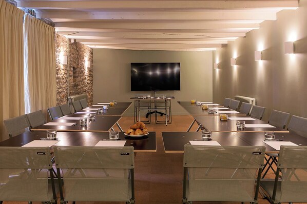 A conference room with a long table, chairs, a television, and a stone wall. - Alfred Hotels Beaune La Madeleine (Beaune)
