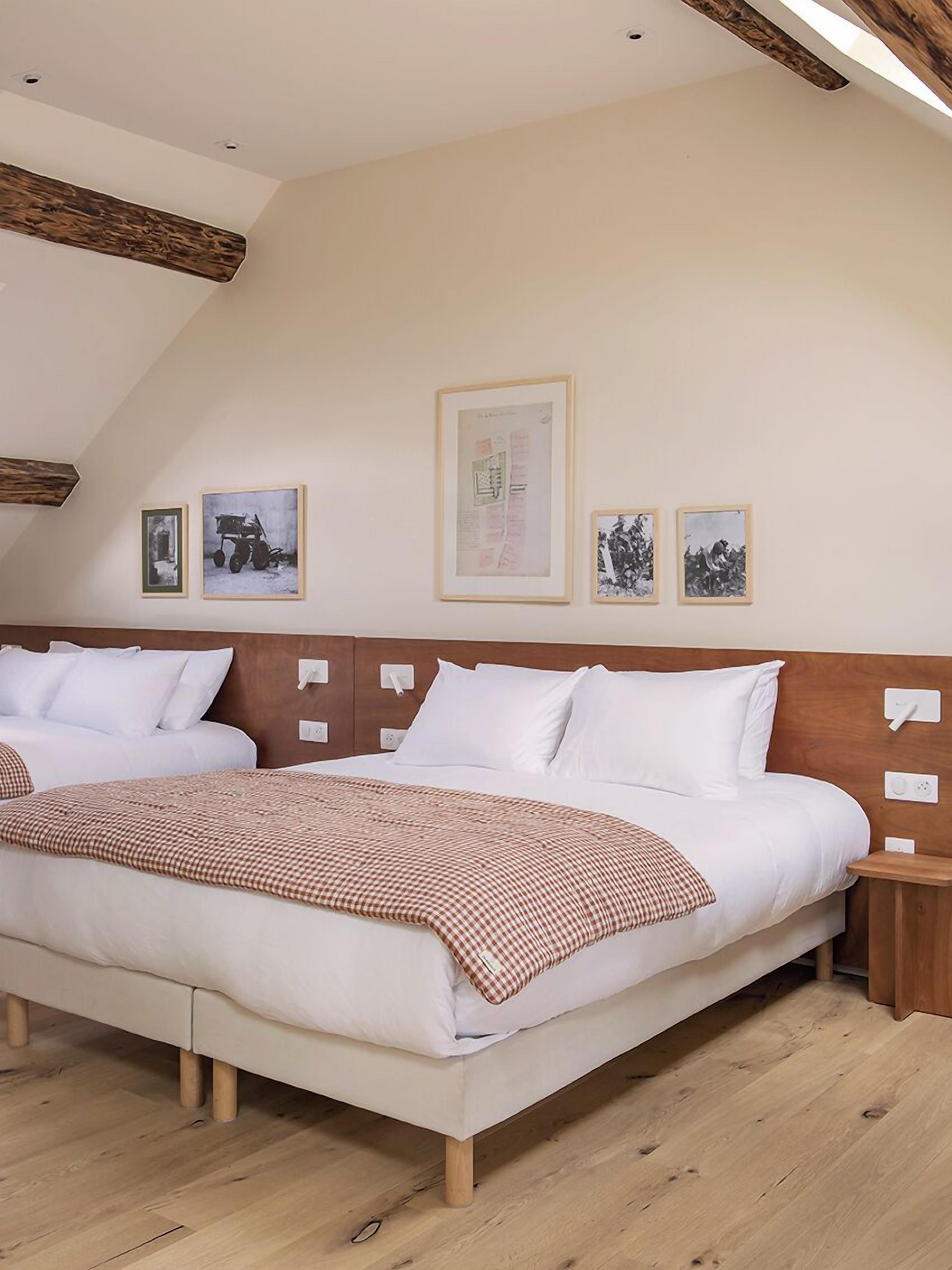 Un grand lit avec du linge de lit blanc et un couvre-lit à carreaux, une tête de lit en bois et un plafond avec des poutres apparentes.