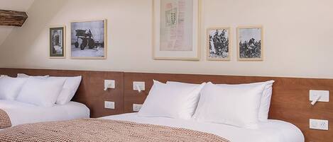 A large bed with white linens and a checkered throw, wooden headboard, and a ceiling with exposed beams.