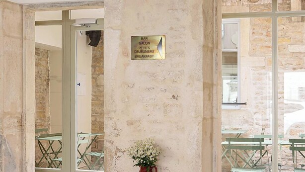 A stone-walled interior with a wooden table and a vase of flowers. A sign indicates a bar, salon, and breakfast area. - Alfred Hotels Beaune La Madeleine (Beaune)