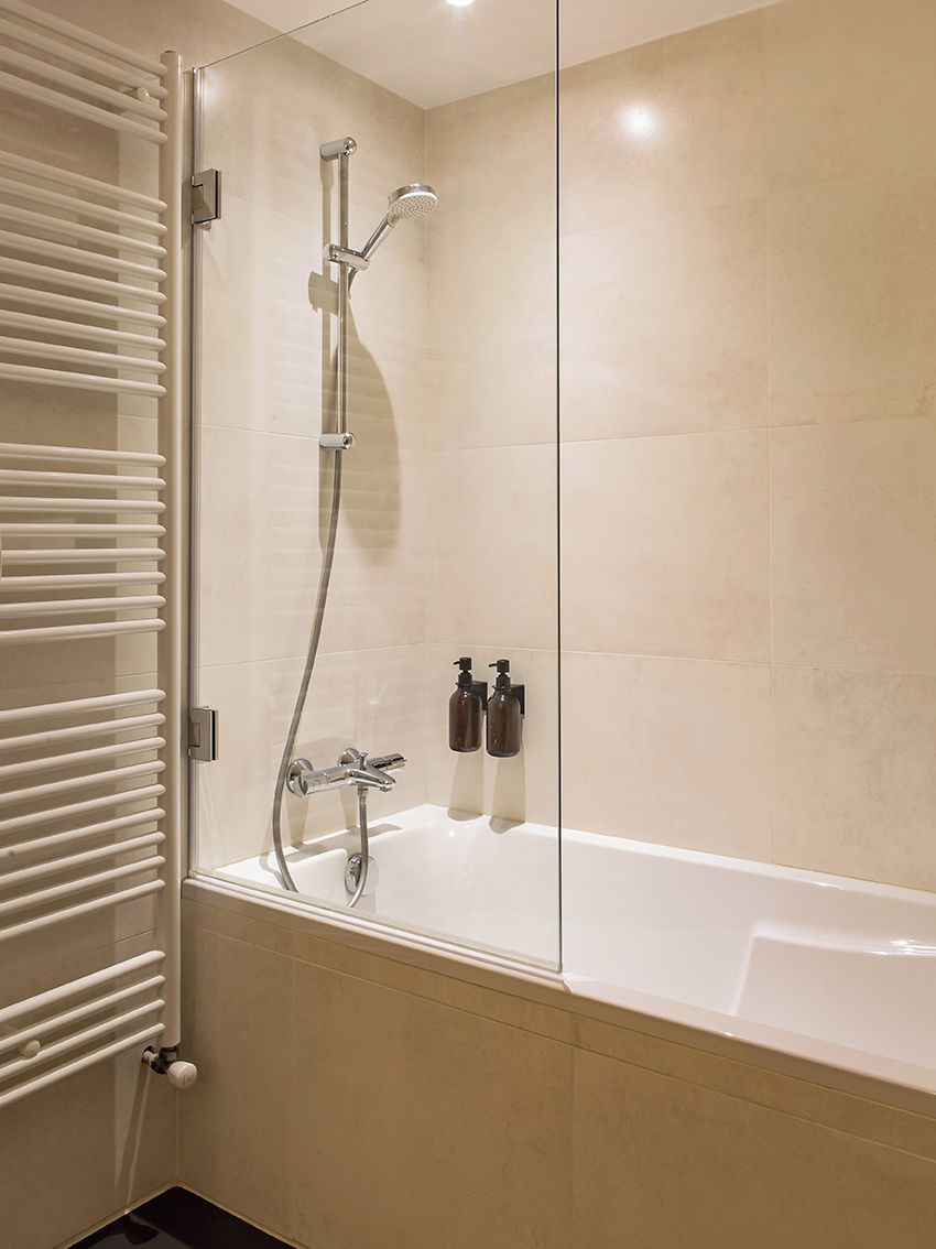 A modern bathroom with a glass-enclosed shower, a white bathtub, and a built-in towel rack.
