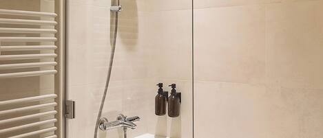 A modern bathroom with a glass-enclosed shower, a white bathtub, and a built-in towel rack.
