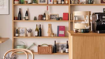 A room with a wooden table, chairs, a coffee machine, and shelves with wine bottles and books.