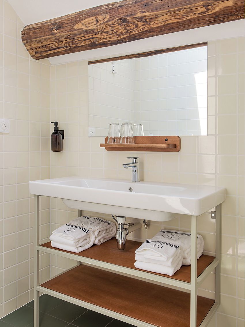 A bathroom with a white sink, wooden shelf, and towel racks.