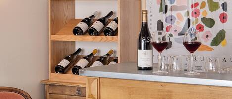 A wooden bar area with wine bottles and glasses, a chair, and a colorful abstract painting.