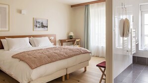 A hotel room with a large bed, a bedside table with a lamp, a small stool, and a view of the outside through a glass door. - Alfred Hotels Beaune La Madeleine (Beaune)