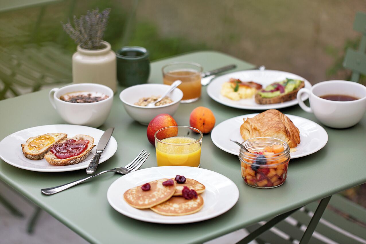 A table set with breakfast items including toast, pancakes, fruit, and a croissant.
