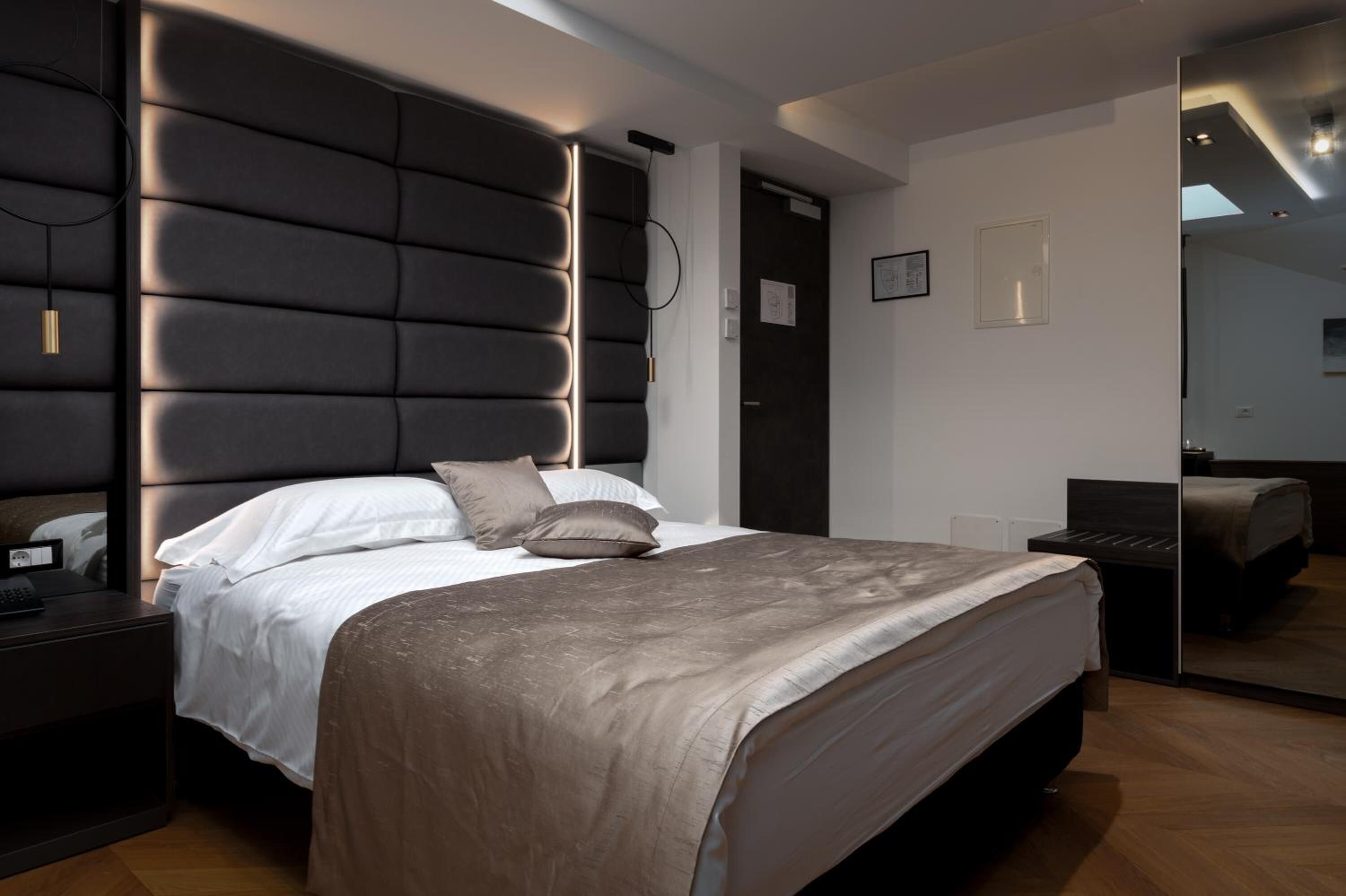 A modern bedroom with a large bed, a bedside table, a wall-mounted light, and a mirror.