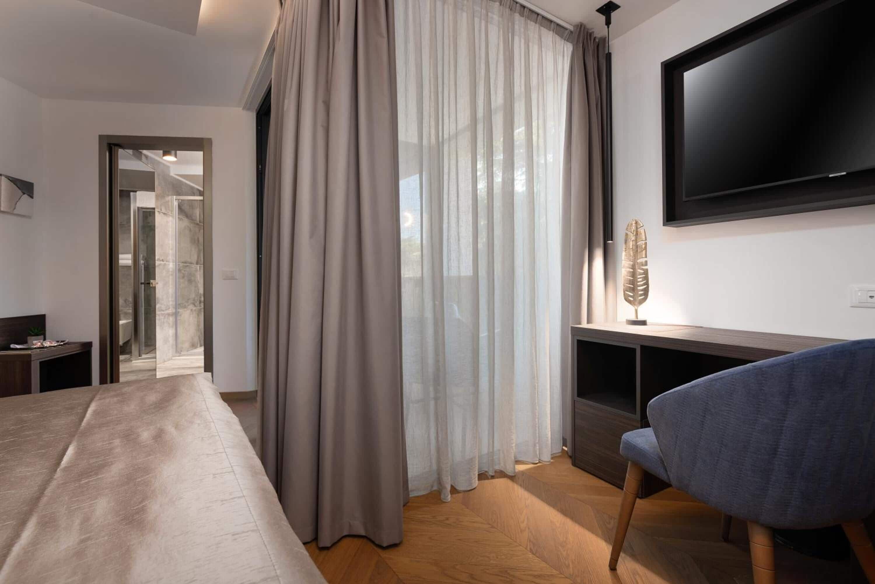 A modern hotel room with a large bed, a TV mounted on the wall, a desk, and a chair.