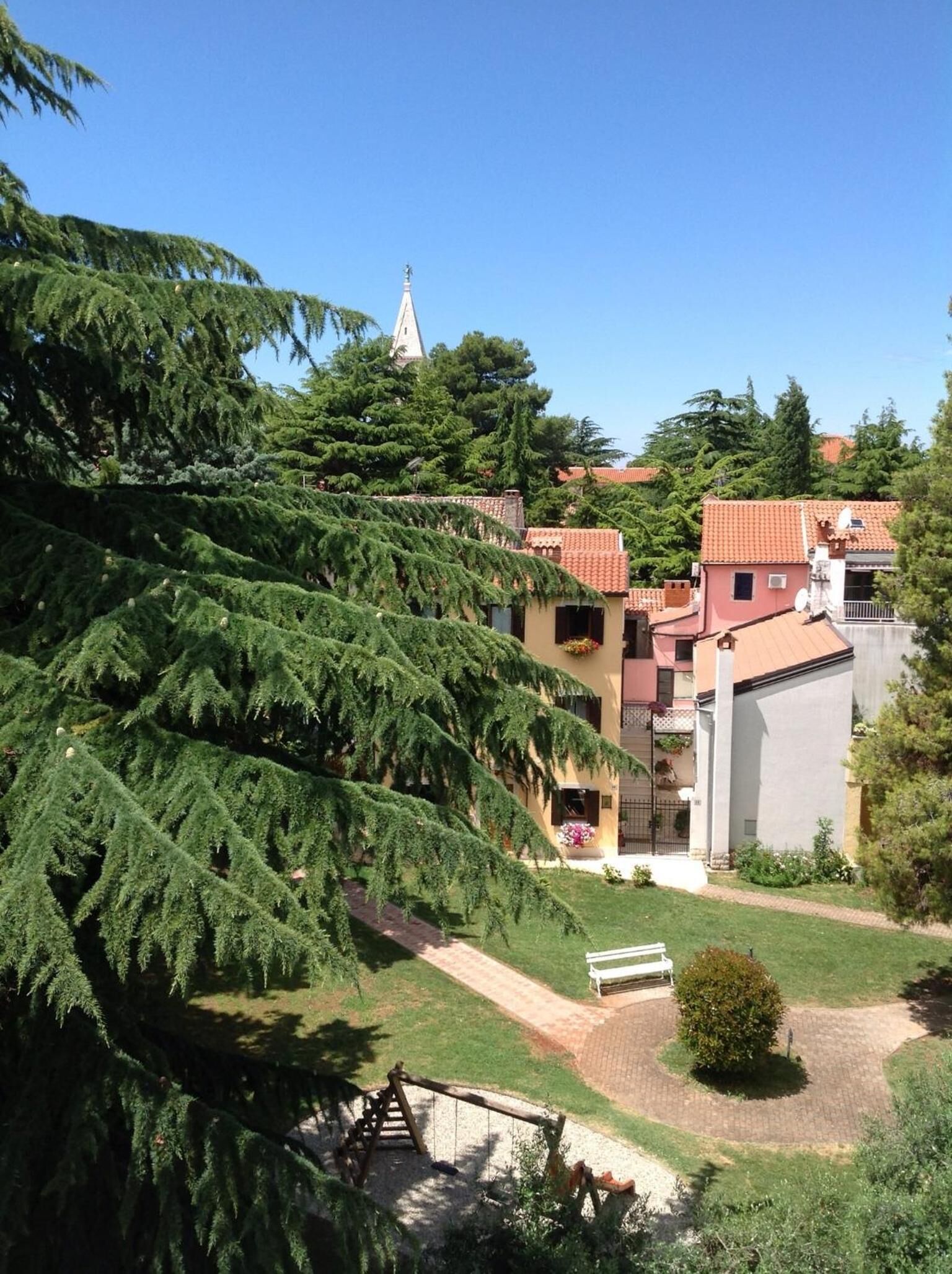 Zona residencial con casas adosadas, una aguja de iglesia y un parque infantil con columpios.