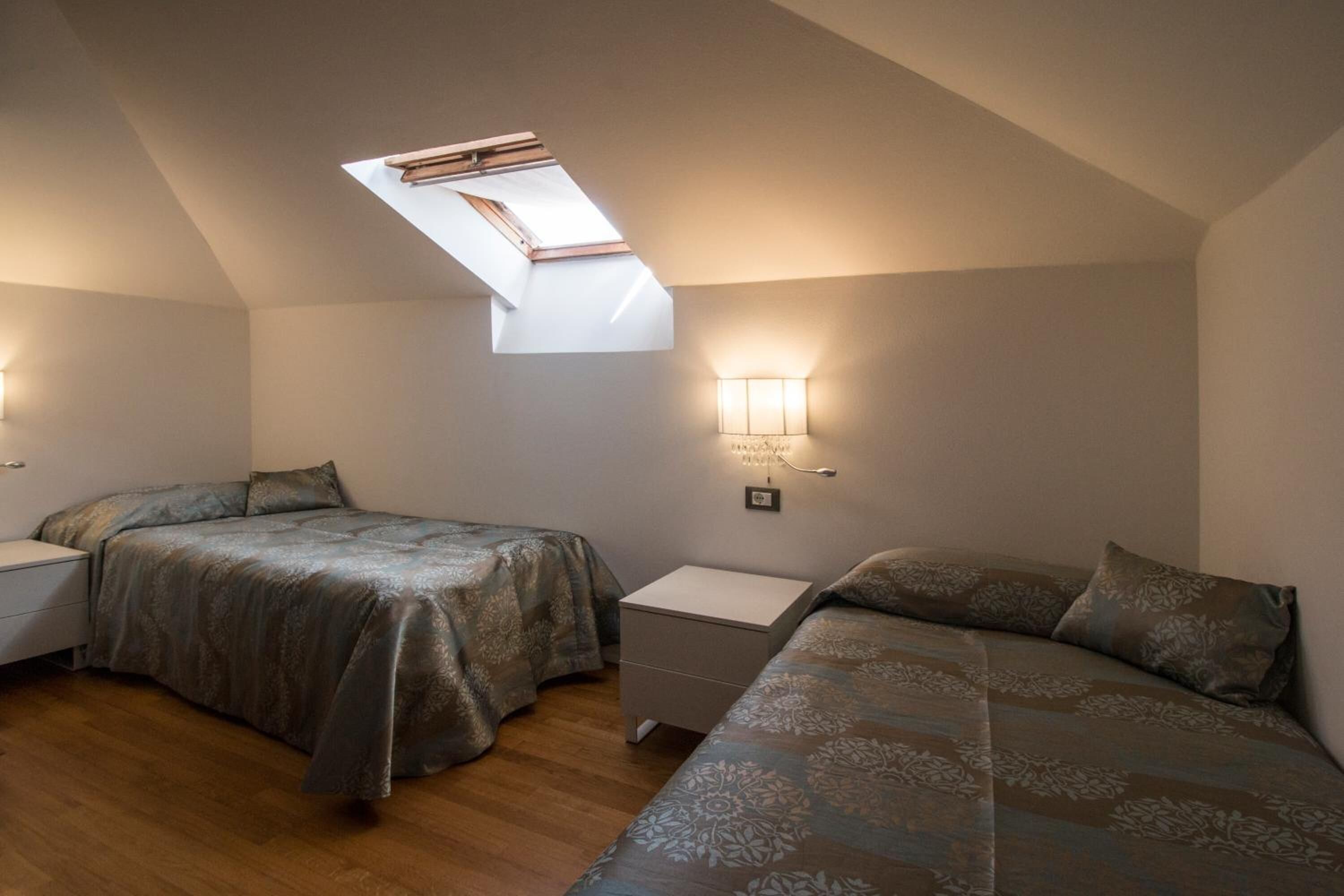 A bedroom with two beds, a skylight, and bedside lamps.