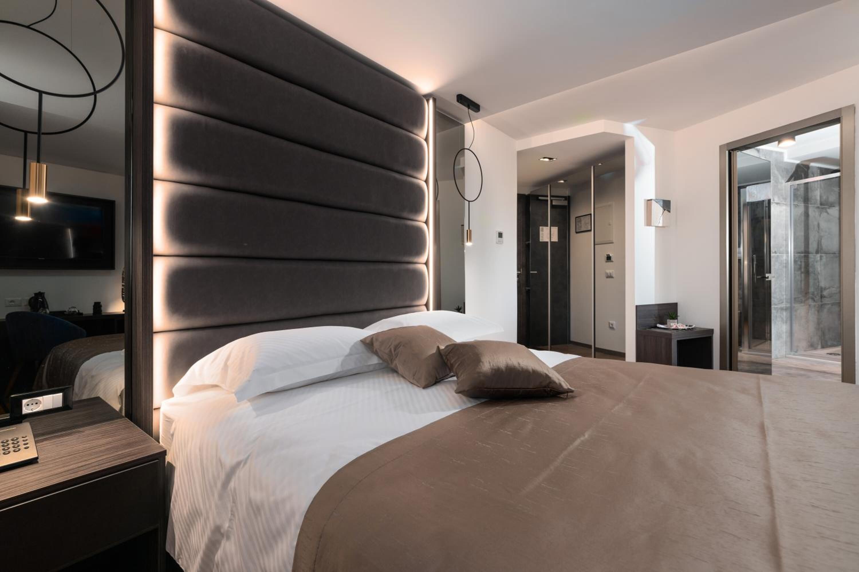 Ett modernt hotellrum med en stor säng, ett sängbord med en lampa, en platt-TV och en stor spegel.