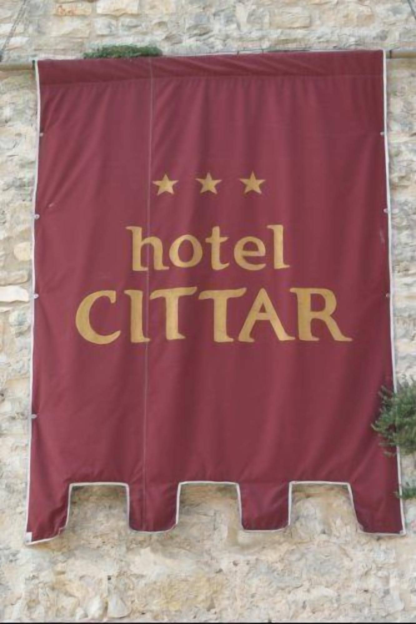 A maroon banner with the text "hotel CITTAIR" and three stars above it, mounted on a stone wall.