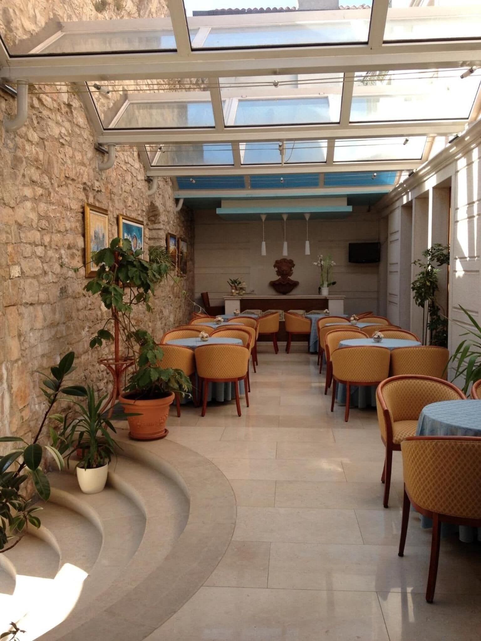 A restaurant with a stone wall, potted plants, and a central seating area with tables and chairs.