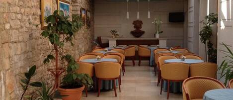 A restaurant with a stone wall, potted plants, and a central seating area with tables and chairs.
