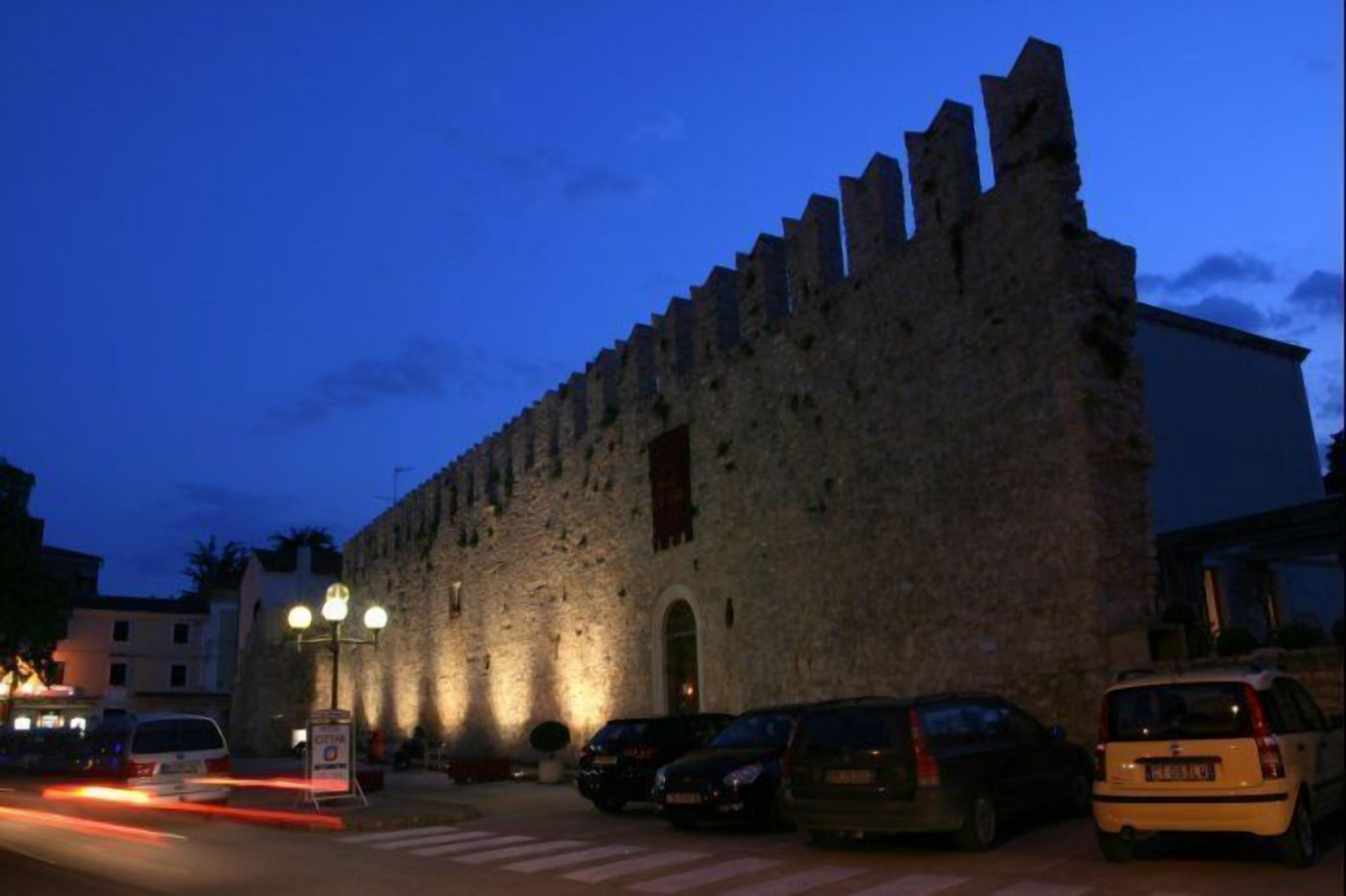 Un edificio histórico de piedra con un gran arco de entrada, varias ventanas y un asta de banderas.